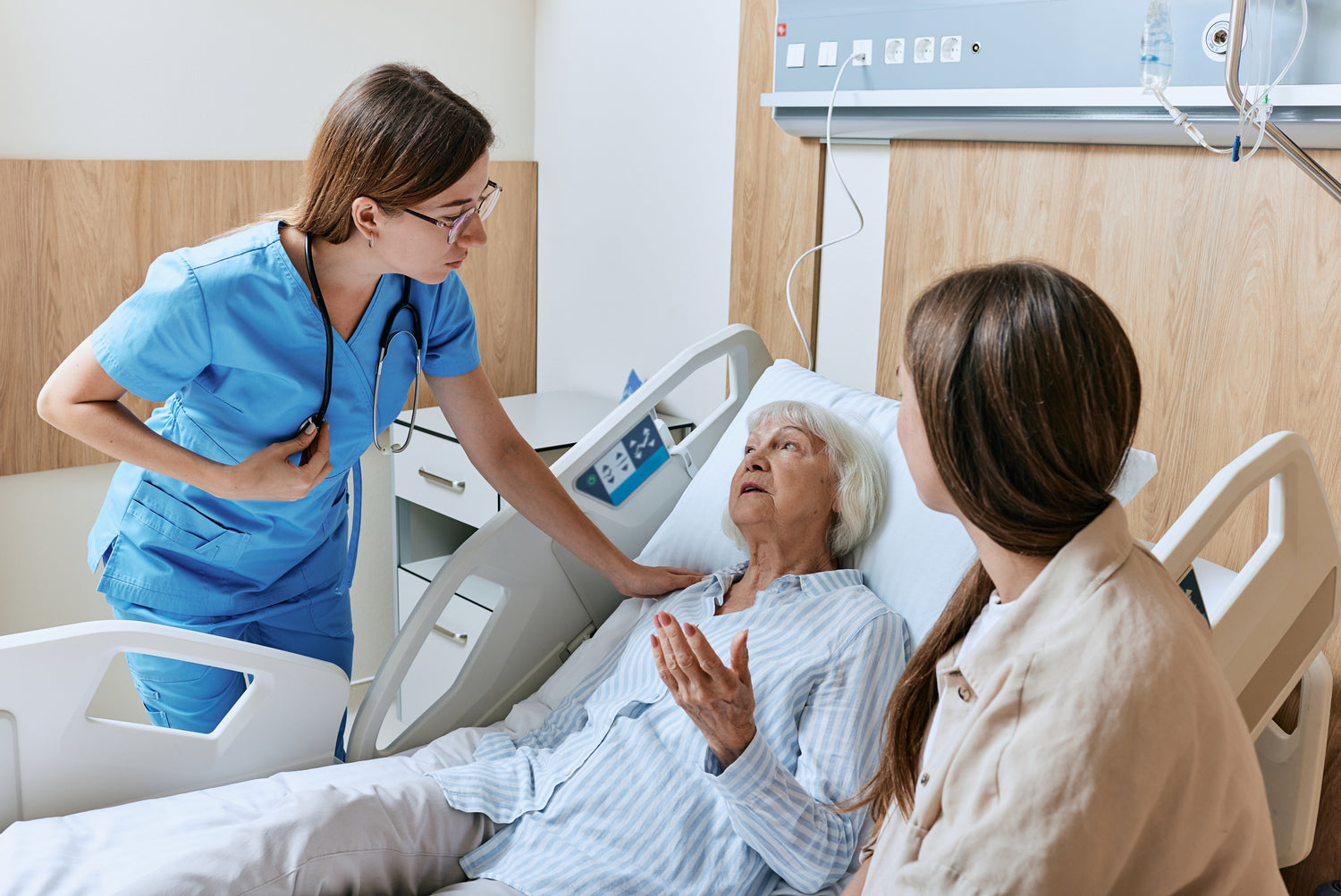 Woman in hospital bed speaking with healthcare provider, accompanied by family member