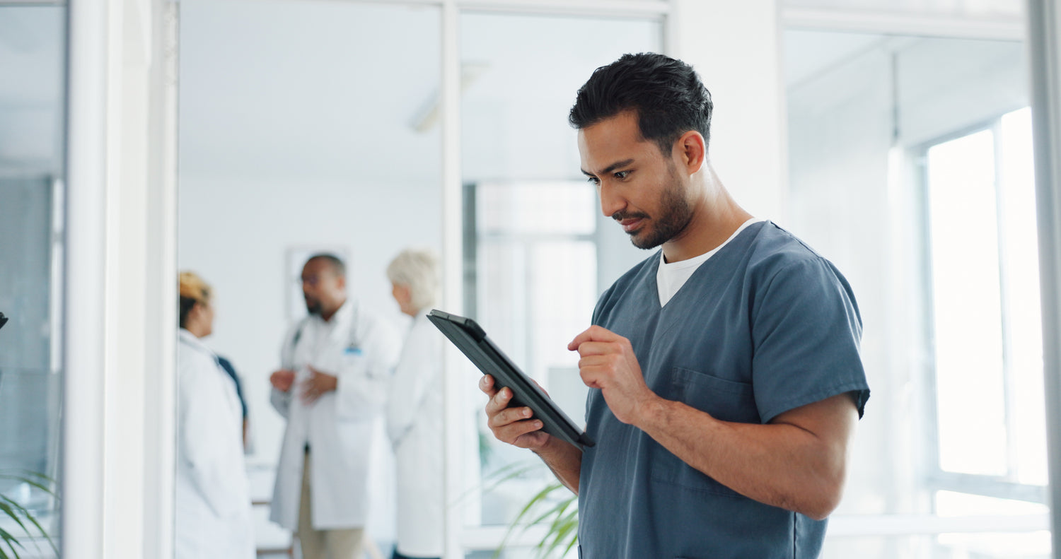 Man in scrubs working on tablet; doctors in labcoats conversing in background