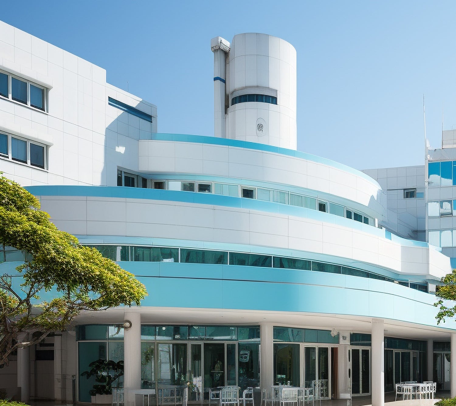 A large white hospital building featuring a blue roof, set against a clear sky, showcasing modern architectural design.